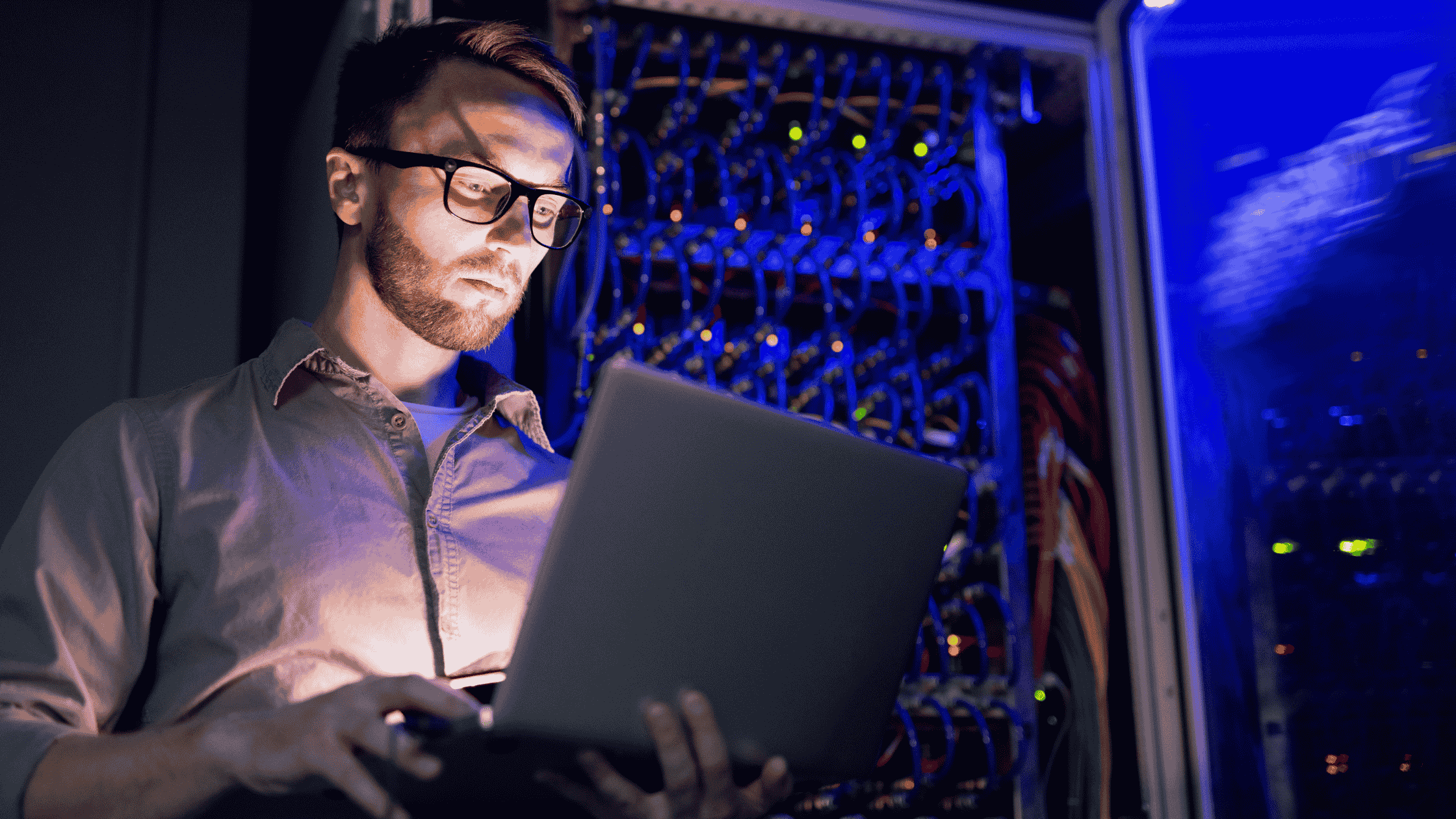 Man working on a laptop in a server room representing how the ChatGPT advertising model works through AI systems, data processing, and machine learning infrastructure.